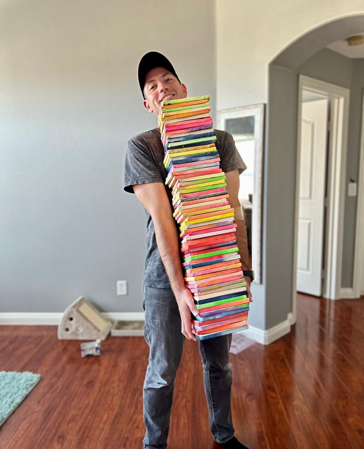 Matthew Mandala holding a tall stack of colorful original paintings